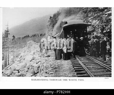 . English: Passengers standing outside of White Pass and Yukon Railroad train car, White Pass, ca. 1907 . English: Caption on mount: Railroading Through the White Pass, Alaska On verso of image: ca. 1907 White Pass is located at the 2900 foot level on the Alaska-Canada boundary, 4 miles northeast of Mount Cleveland and 13 miles northeast of Skagway, in the Coast Mountains. This pass was on one of the principal routes to the Yukon taken by the prospectors during the Klondike Gold Rush 1897-1900. Although the White Pass route was less direct than the favorite but steeper Chilkoot Pass route, it  Stock Photo