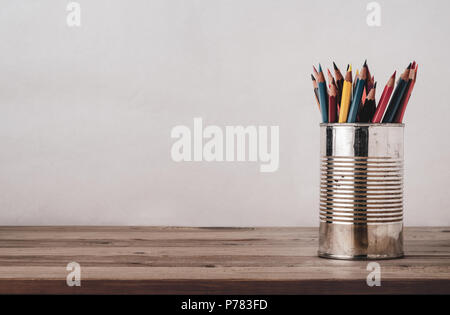 A variety of coloured pencils in an old metal tin on a wood plank desk with copy space to left and above. Filtered for retro effect. Stock Photo