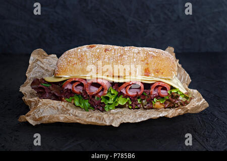 Sandwich of crispy ciabatta with ham, cheese and lettuce leaves on a dark background. Stock Photo