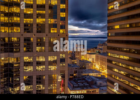 empty office block windows at night with empty desks and computers visible through the glass Stock Photo