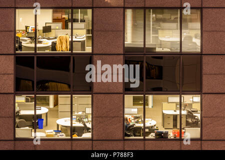Close up of empty office block windows at night with empty desks and computers visible through the glass Stock Photo