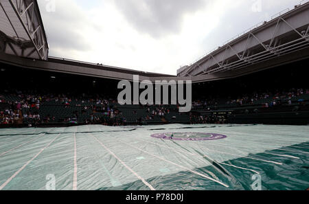 Ground staff put the covers on centre court as rain stops play on day three of the Wimbledon Championships at the All England Lawn Tennis and Croquet Club, Wimbledon. Stock Photo
