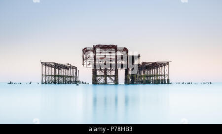 Minimalistic West Pier in Brighton, East Sussex, at sunrise and reflected in a calm sea with beautiful pastel shades in a cloudless sky Stock Photo