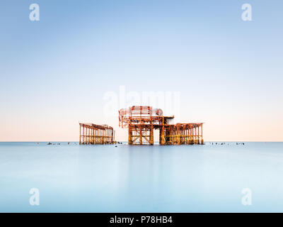 Minimalistic West Pier in Brighton, East Sussex, at sunrise and reflected in a calm sea with beautiful pastel shades in a cloudless sky Stock Photo