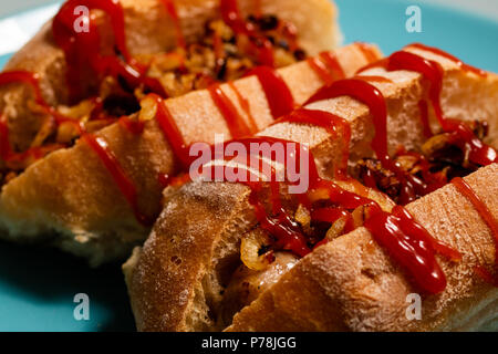 A delicious looking sausage sandwich cooked in a homemade bread roll with fried onions and ketchup Stock Photo