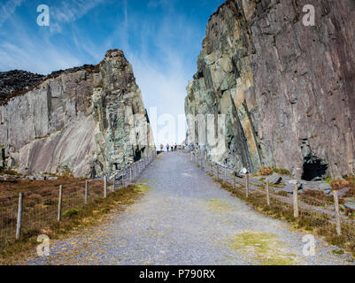 Four walkers in the distance walking on the path from Nant Peris through the Dinorwic slate quarry and towards Llanberis in Snowdonia, North Wales Stock Photo