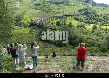 Tourists photograph the Jacobite Express, (Hogwarts Express) as it crosses the Glenfinnan Viaduct on route between Fort William and Mallaig. Stock Photo
