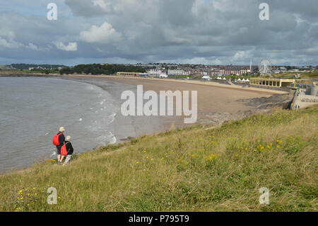 Two people walking along a coastal path above the beach and bay at Barry Island at low tide Stock Photo
