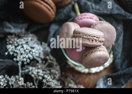 Freshly baked macaroons in wicker basket with handles with small white flowers on wooden background. Selective focus. Stock Photo