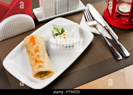 ceramic white plate with pancake  and soft caviar, on table in restaurant Stock Photo