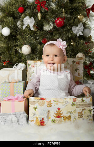 one-year-old little girl solemnize Christmas, sit under Christmas-tree with gift, vertical photo Stock Photo