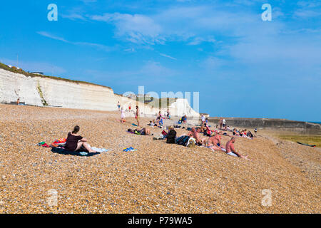 People relaxing and suntanning on the shingle beach in Saltdean with white cliffs in the background, East Sussex, UK Stock Photo