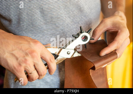 Making holes with puncher in leather workshop. Male hands with eyelet puncher working with piece of material Stock Photo