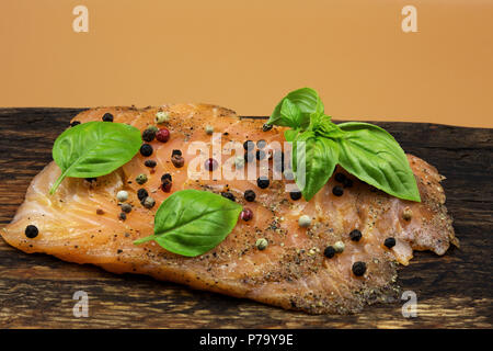 Photo of a piece of smoked salmon, garnished with colorful peppercorns and basil leaves, arranged on an old wooden chopping board with copy space on t Stock Photo