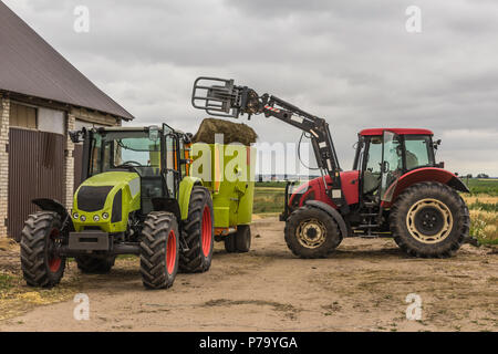 Agricultural machinery and equipment.The tractor with the loader loads a bale of silage in the distributor of mixed fodders for cows.Podlasie, Poland. Stock Photo