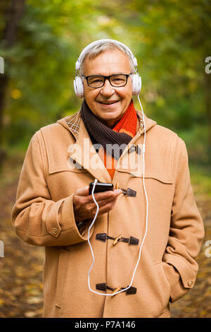 Senior man listening music in park in autumn. Stock Photo