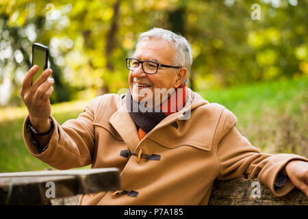 Happy senior man taking selfie in park in autumn. Stock Photo