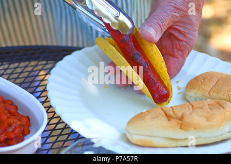 A man makes a taco dog with a dish of chili alongside Stock Photo