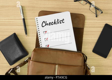 Checklist word written on notebook. Men's leather bag with personal items on wood background. To do list. Stock Photo