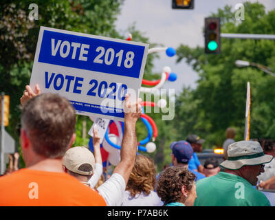Oak Park, Illinois, USA 4th July, 2018. An Independence Day participant holds a sign reminding people to vote in the upcoming 2018 and 2020 elections. Temperatures this 4th of July were well over 90ºF/32ºC with a heat index of over 100ºF. Credit: Todd Bannor/Alamy Live News  Stock Photo