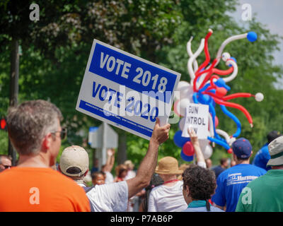 Oak Park, Illinois, USA 4th July, 2018. An Independence Day participant holds a sign reminding people to vote in the upcoming 2018 and 2020 elections. Temperatures this 4th of July were well over 90ºF/32ºC with a heat index of over 100ºF. Credit: Todd Bannor/Alamy Live News Stock Photo