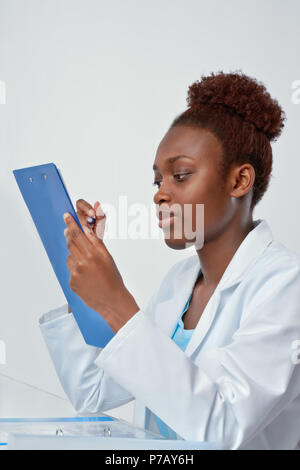 African scientist, medical or or graduate student. Confident young woman wearing lab coat holds a pen and a notepad, focus on the eyes Stock Photo