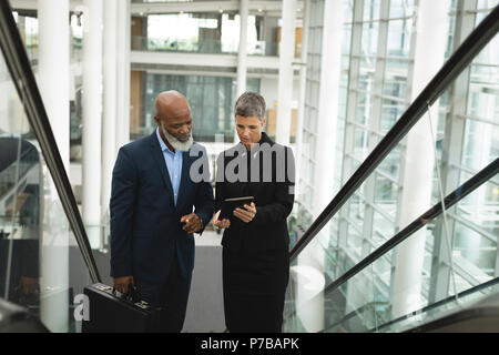 Businesspeople discussing over a tablet while going up on an escalator Stock Photo