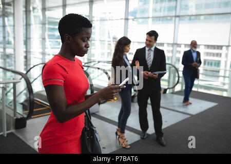 Businesswoman using her phone while colleagues are discussing Stock Photo