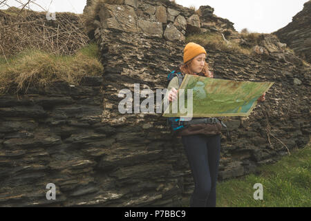 Female hiker leaning against the rock and reading a map Stock Photo