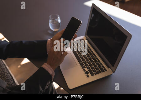 Businesswoman using smartphone while working on laptop Stock Photo