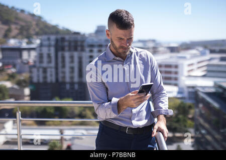Businessman leaning on railing while using mobile phone Stock Photo