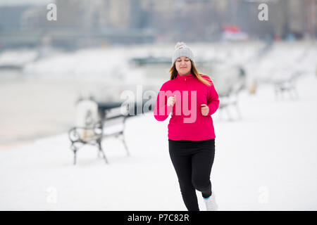 Pretty girl wearing sportswear and running on snow during winter Stock Photo