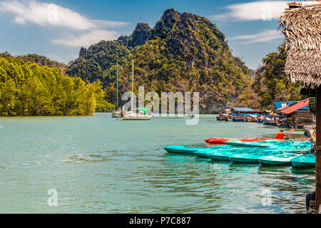 Beautiful scenery of two sailing boats next to a mangrove coastline and many moored kayaks and motorboats at a floating platform with a limestone... Stock Photo