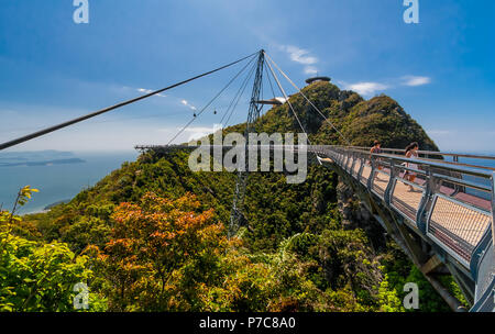 Great scene of 2 visitors walking along the curved pedestrian single-pylon Langkawi Sky Bridge & admiring the view. In the backdrop 2 gondolas are... Stock Photo