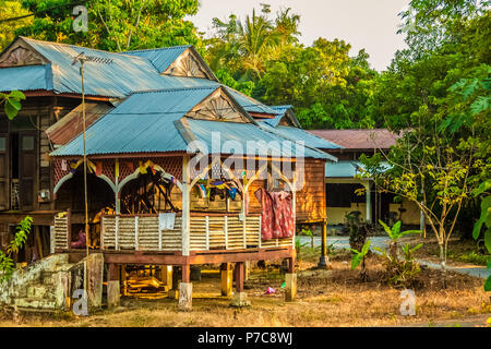 A traditional wooden Malay house on stilts with a tropically-suited roof, clothes drying on a clothesline; home of local residents on Langkawi Island... Stock Photo