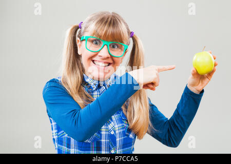 Studio shot portrait of happy nerdy woman who is pointing at apple Stock Photo