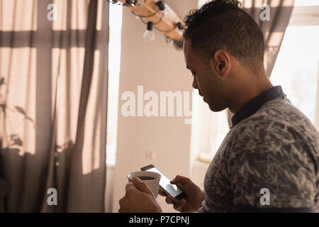 Man using mobile phone while having coffee in kitchen Stock Photo