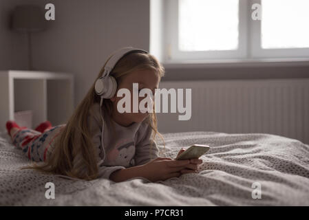 Girl listening music on mobile phone with headphones in bedroom Stock Photo