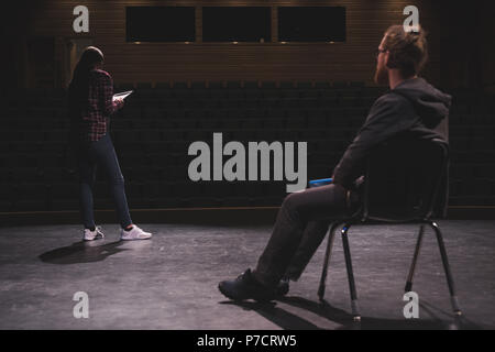 Female actress reading script while male actor looking at her on stage Stock Photo