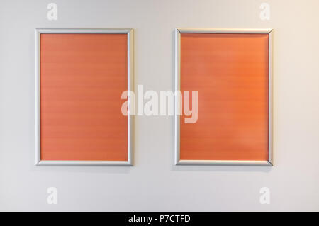 Two picture frames with orange copy space hanging on white wall Stock Photo