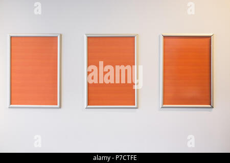 Three picture frames with orange copy space hanging on white wall Stock Photo