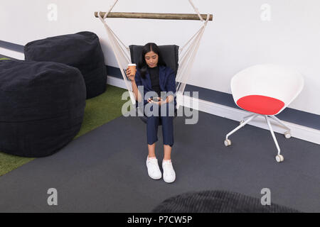 Female executive having coffee while using digital tablet in office Stock Photo