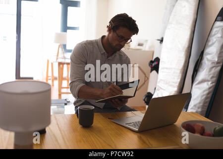 Man writing on a diary while using laptop Stock Photo