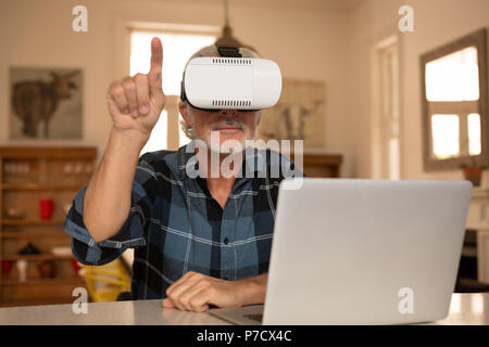 Senior man using virtual reality headset with laptop in kitchen Stock Photo