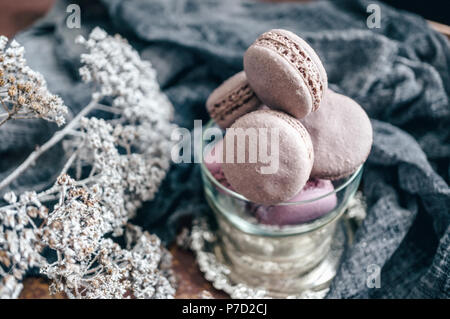 Freshly baked macaroons in wicker basket with handles with small white flowers on wooden background. Selective focus. Stock Photo