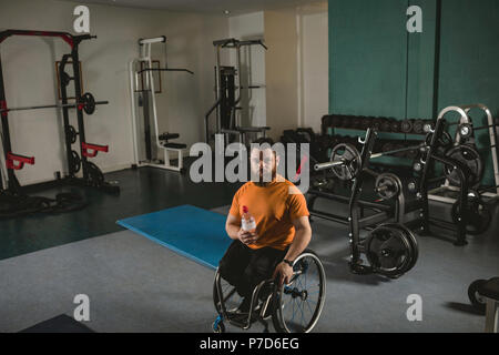 Handicapped man on wheelchair with water bottle in gym Stock Photo