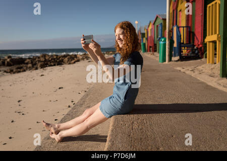 Woman clicking photo of sea with mobile phone at beach Stock Photo