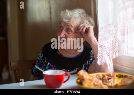An elderly woman sitting at the table drinking tea with pies. Stock Photo