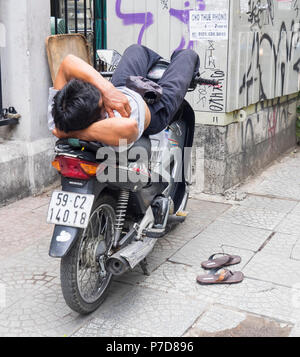 A Vietnamese man taking a nap on a motorcycle in Ho Chi Minh City, Vietnam. Stock Photo