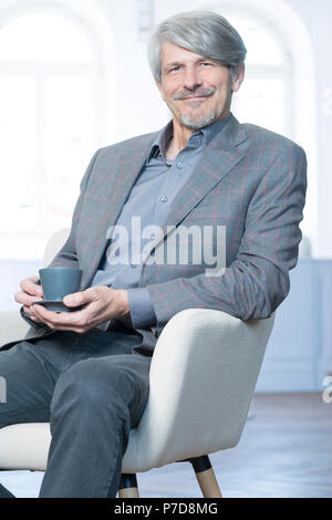 Man sits in his office chair with a coffee cup Stock Photo